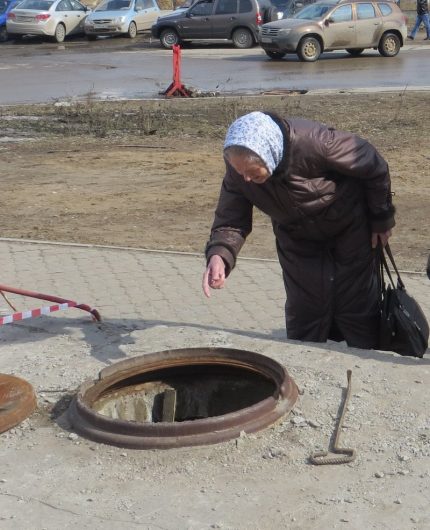 Възрастна жена гледа в канализационен кладенец
